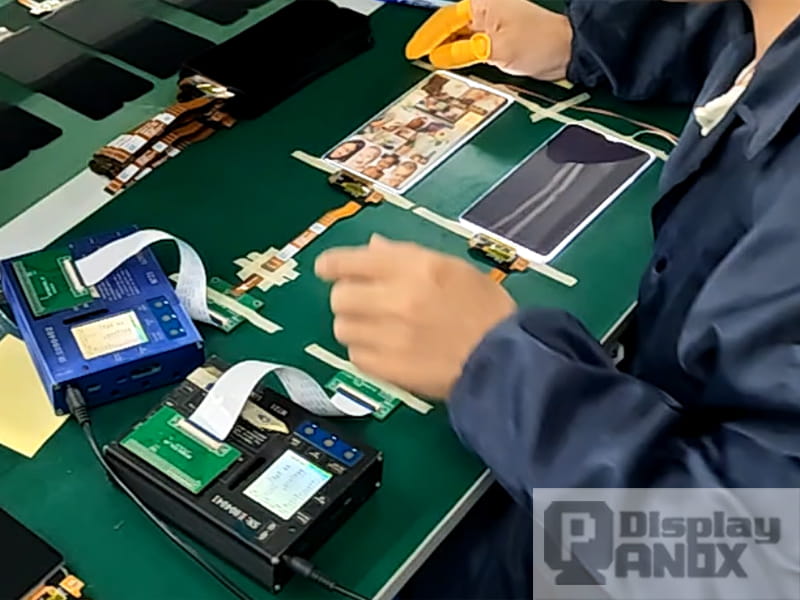 Technician testing phone display panels and flex cable connections at Panox Display production line